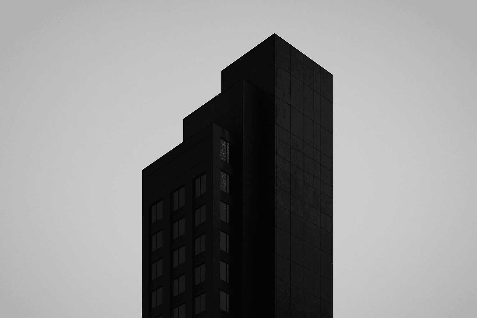 Monochrome architectural photograph of an abstract stepped tower massing at dusk, near-black facade with a steel-blue rim light